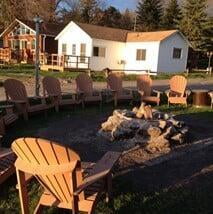 A fire pit surrounded by chairs, with a cottage in the background.