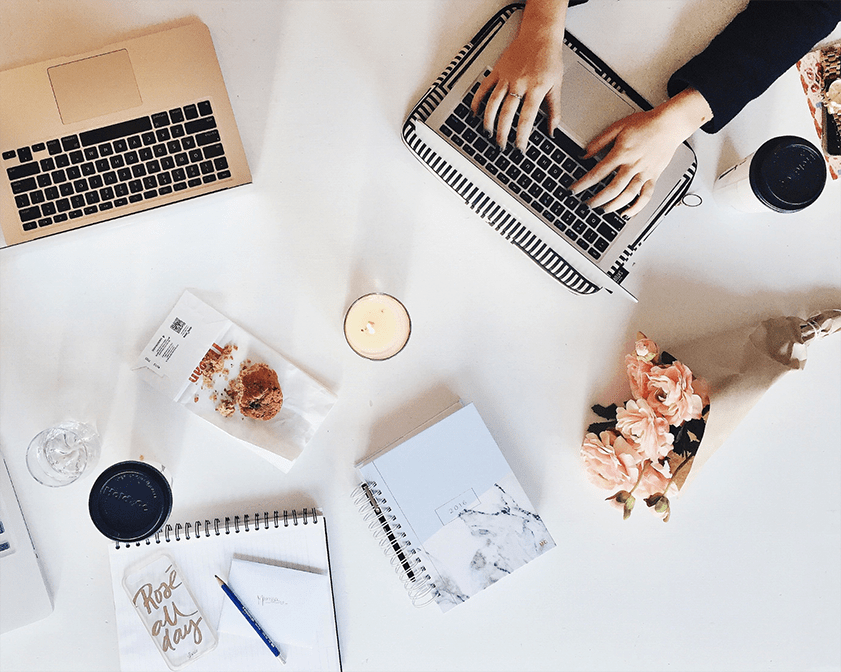 Ceiling view of a table with flowers, a candle and hands typing on a laptop
