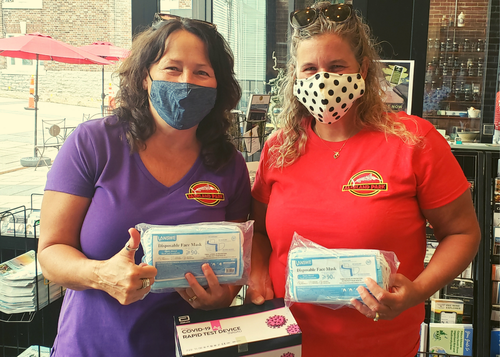 Two staff members from Merland Park holding up masks and rapid test kits and giving the thumbs up
