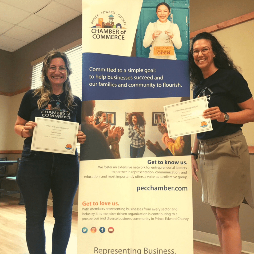 Two staff members standing proudly in front of an informative banner and holding training certificates